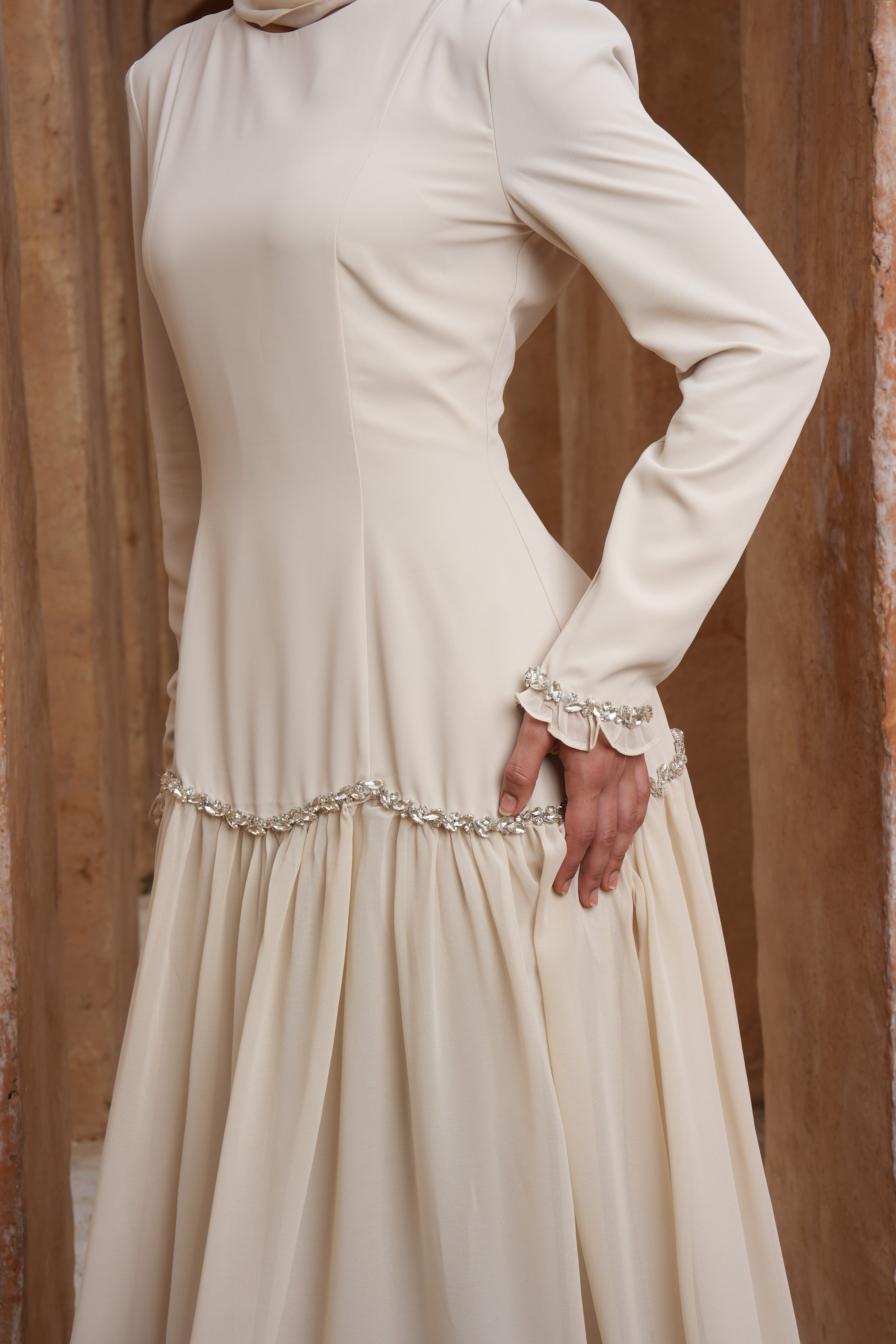 Beige long-sleeve dress with decorative waistband against a wooden background