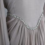 Close-up of a draped taupe-gray evening gown with a sparkling silver rhinestone waistband.