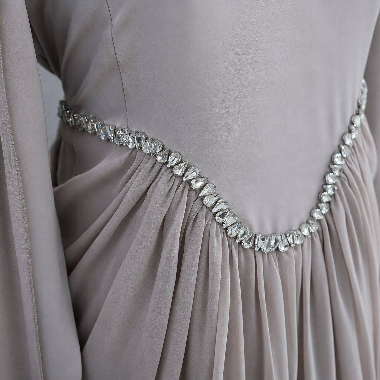 Close-up of a draped taupe-gray evening gown with a sparkling silver rhinestone waistband.