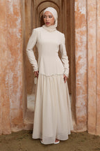 Woman in a long, light-colored dress standing in an arched doorway with a warm-toned wall.