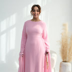 Woman wearing a pink dress standing in a bright room with a plant in the background