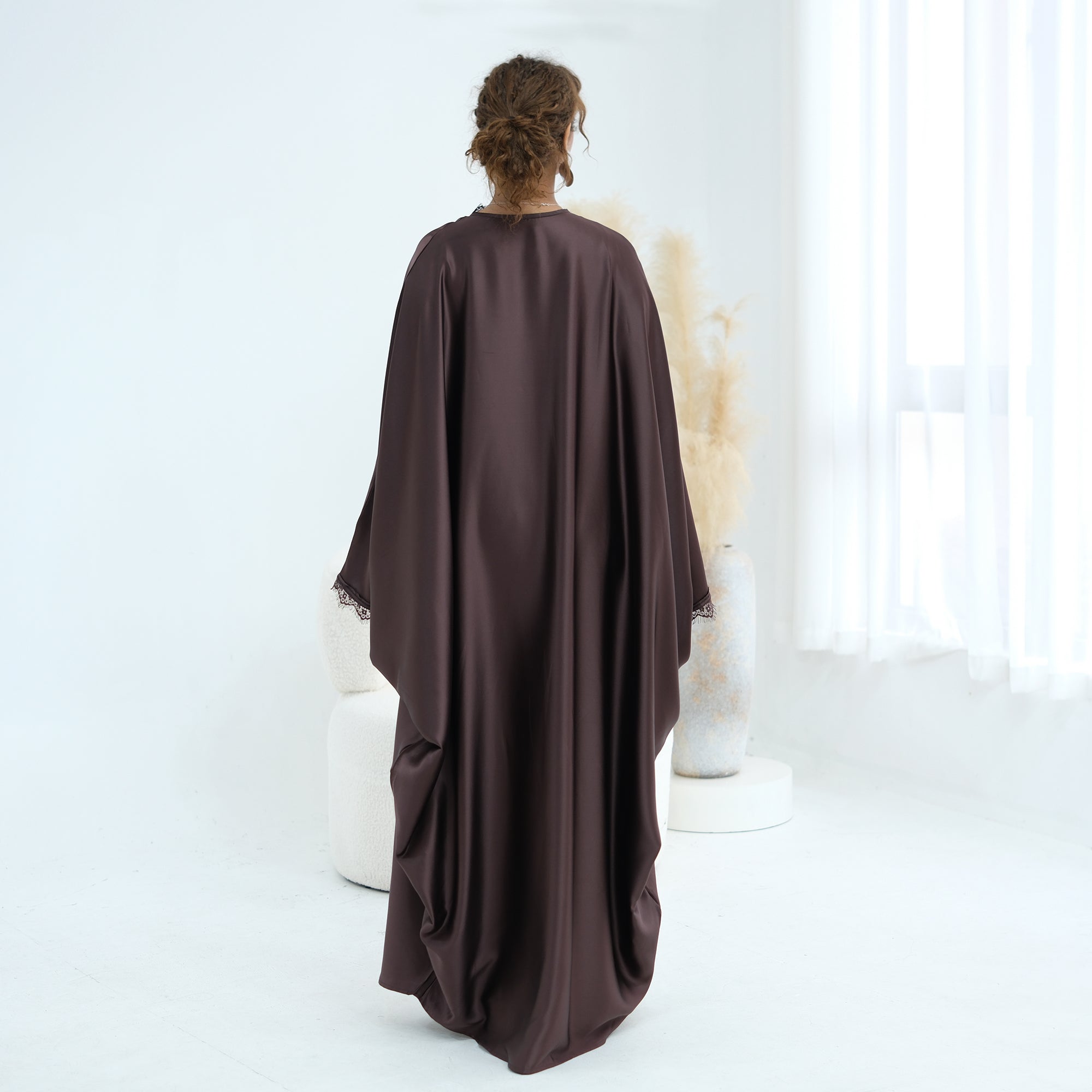 Person wearing a brown abaya sitting on a white chair in a minimalistic room.
