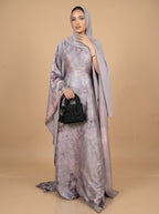 Woman wearing a long, light-colored dress with a matching headscarf against a beige background