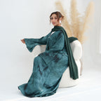Woman in a teal dress sitting on a white chair with a neutral background