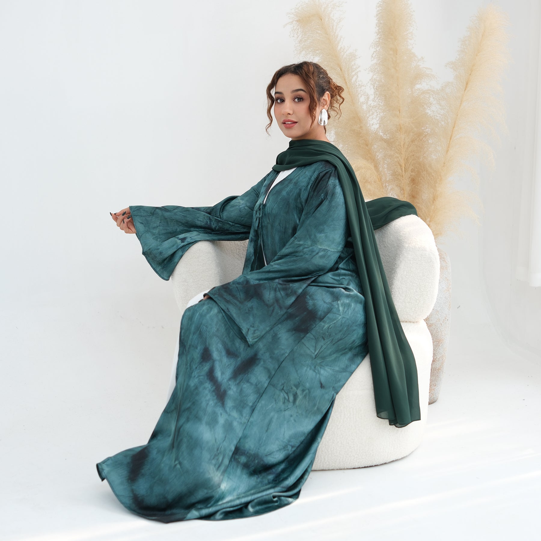 Woman in a teal dress sitting on a white chair with a neutral background