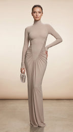 Woman wearing a long, beige dress with a high neckline against a neutral background