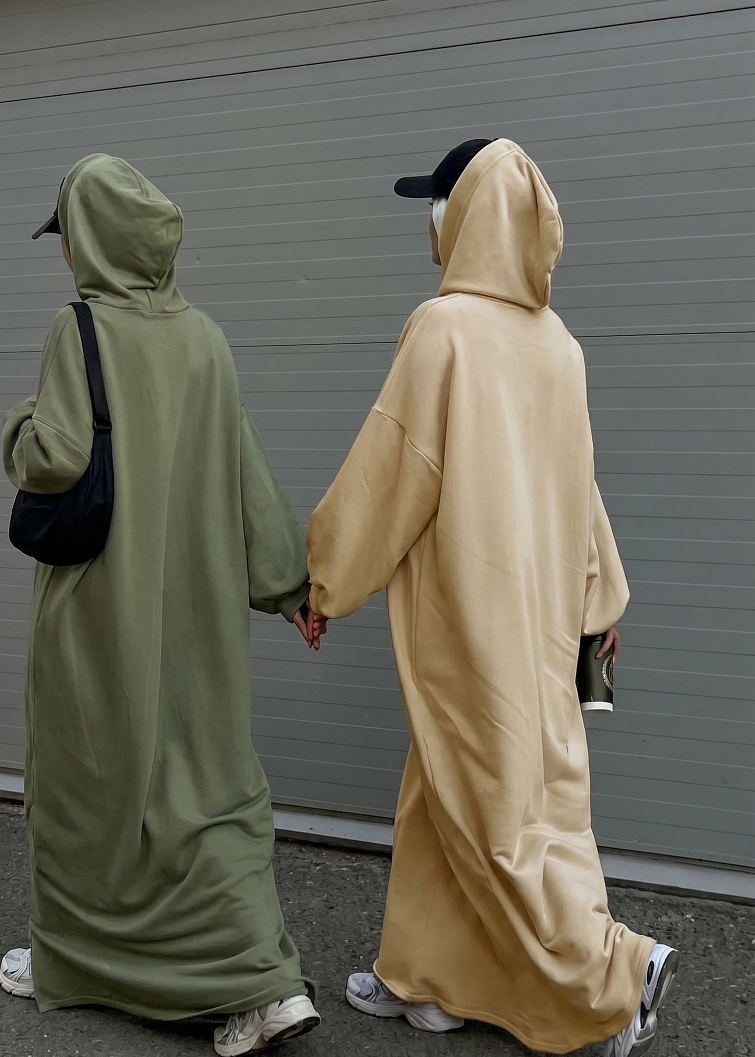 Two people wearing long, hooded cloaks walking side by side on a street.