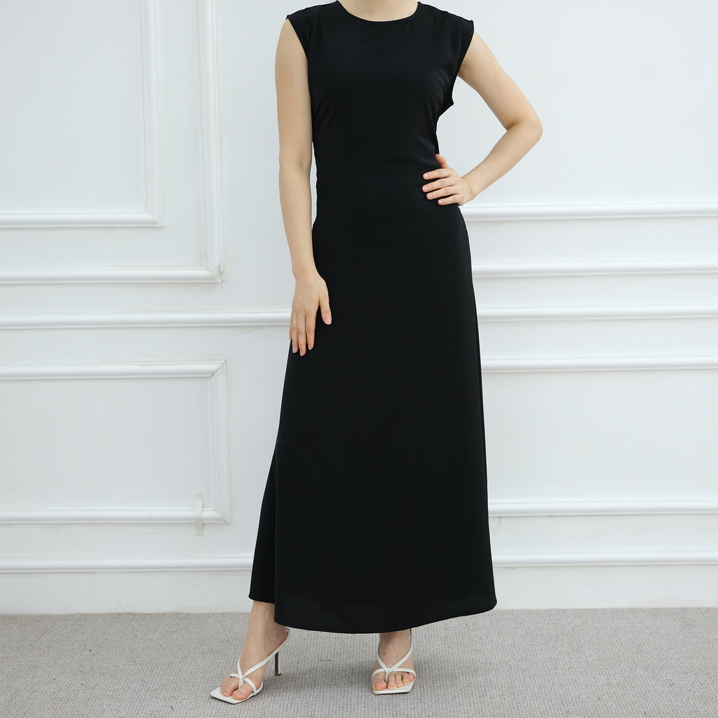 Black sleeveless dress worn by a model against a white wall.