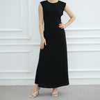 Black sleeveless dress worn by a model against a white wall.