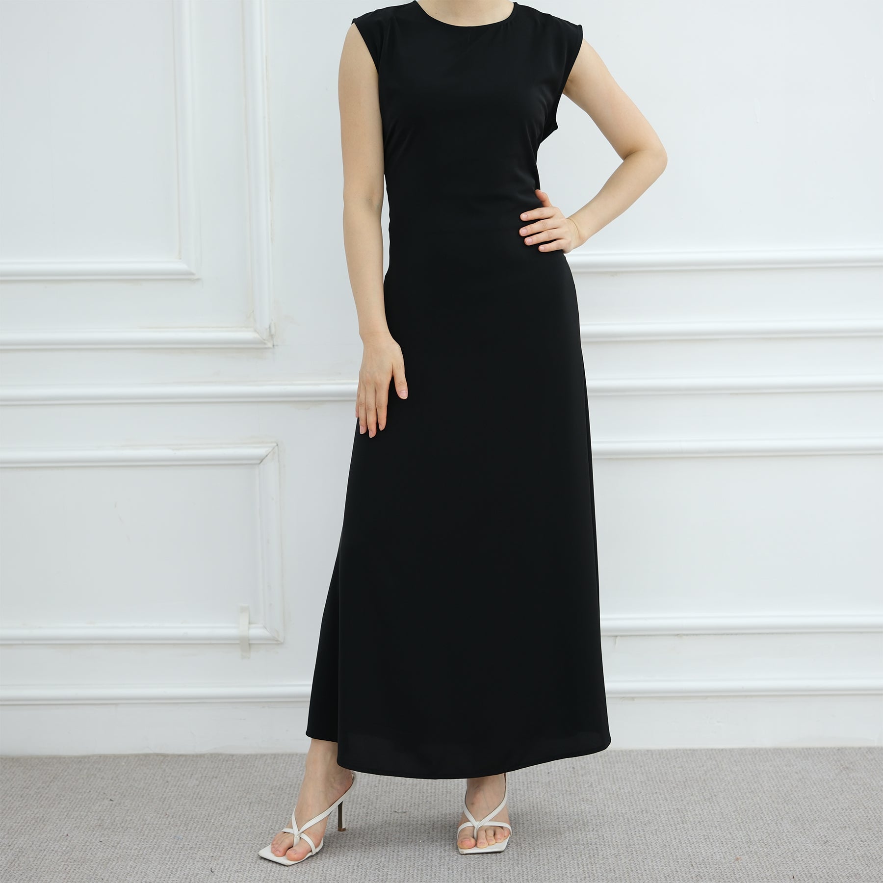 Black sleeveless dress worn by a model against a white wall.