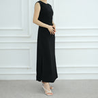 Person wearing a black sleeveless dress against a white paneled wall.