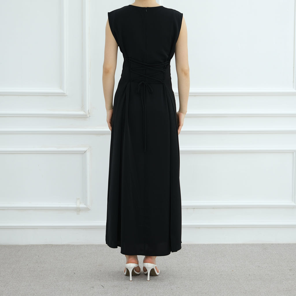 Person wearing a black sleeveless dress against a white paneled wall.