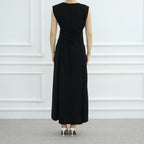 Person wearing a black sleeveless dress against a white paneled wall.