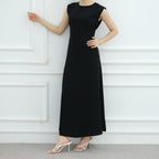 Person wearing a black dress standing against a white paneled wall.