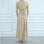 Beige long dress on a mannequin against a white paneled wall.