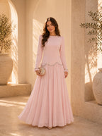 Woman in a pink dress standing in a sunlit outdoor setting with architectural elements.