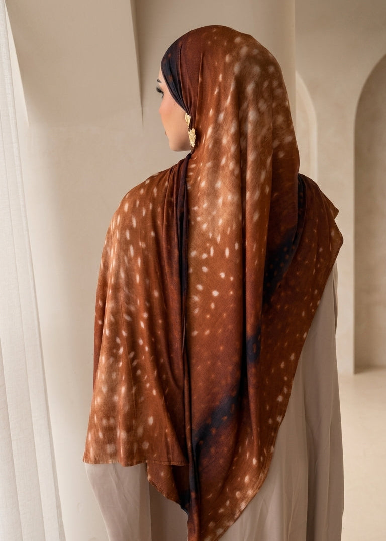 Person wearing a brown scarf with white patterns in a neutral setting
