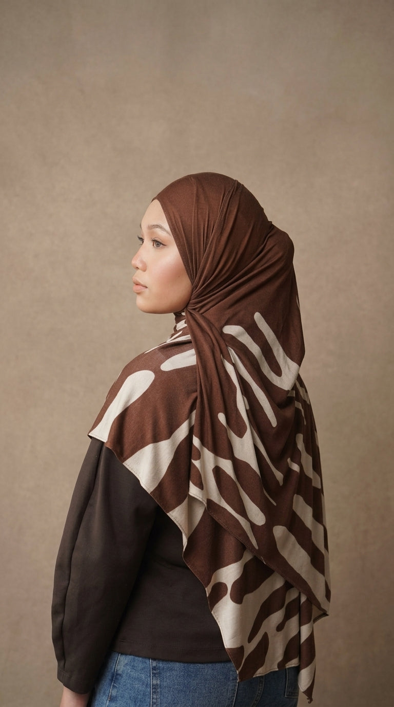 Woman wearing a brown and beige patterned hijab against a plain background