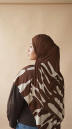 Person wearing a brown and beige patterned hijab against a beige background