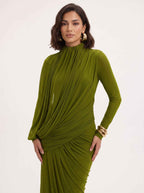 A woman modeling a draped olive green long-sleeve dress with a high mock neck and gathered pleated detailing, set against a plain light background.