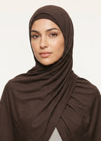 Woman wearing a brown hijab against a beige background