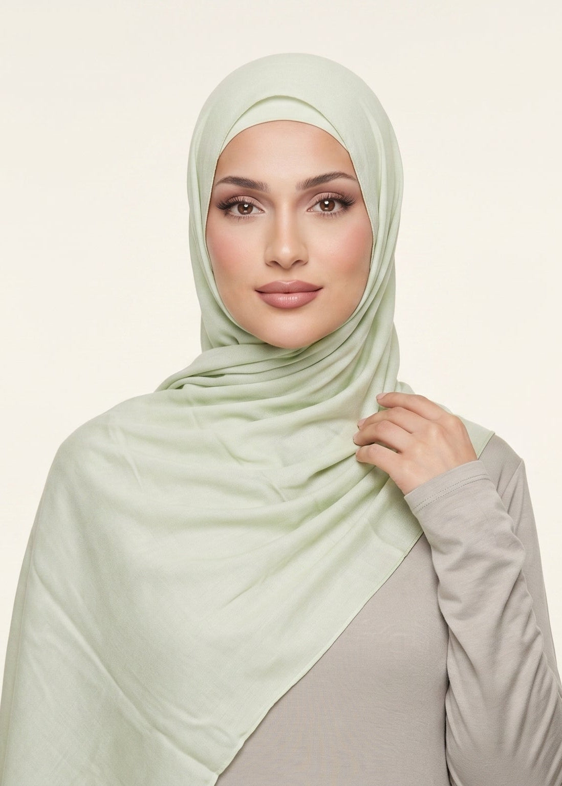 Woman wearing a light green hijab against a plain background