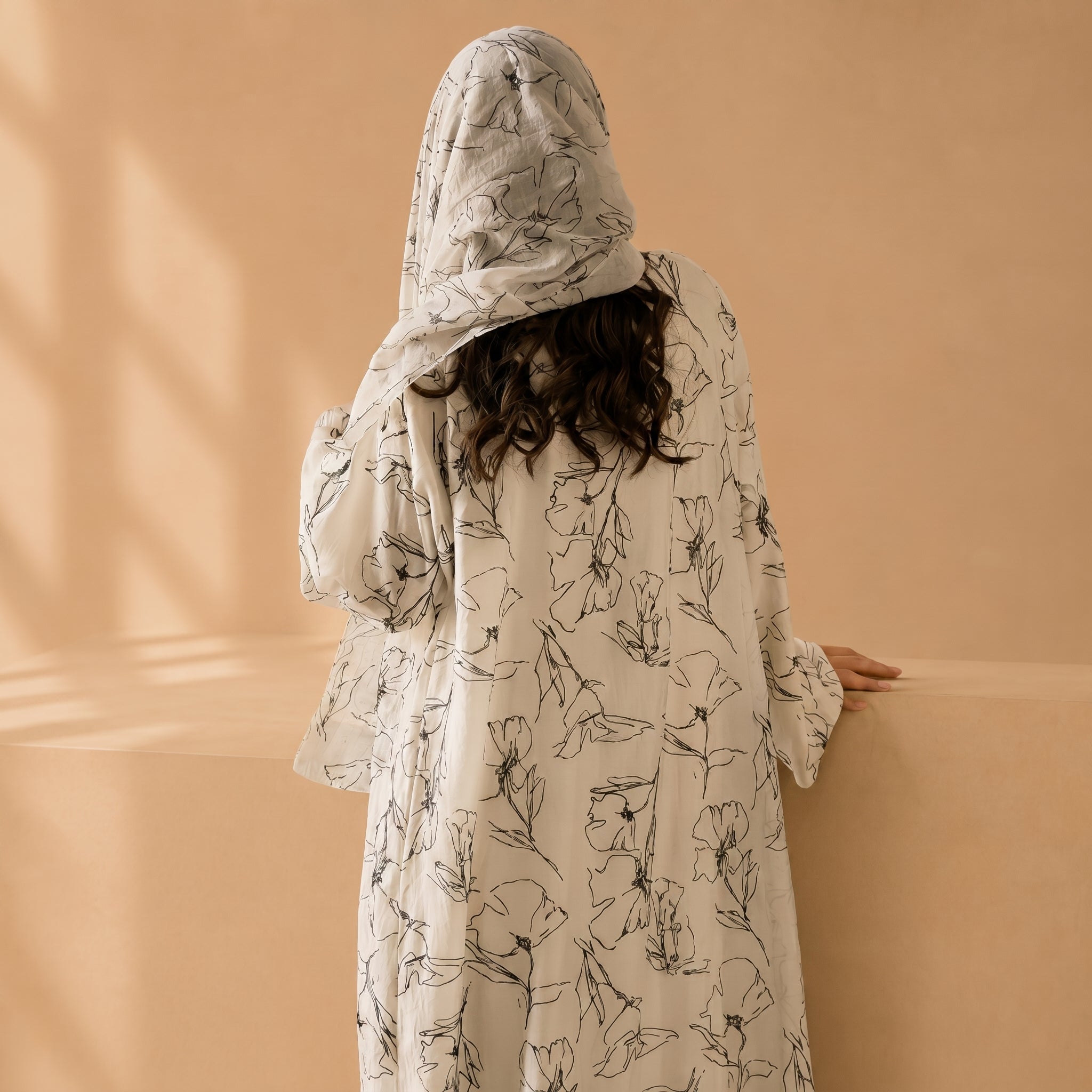 Person wearing a floral-patterned hooded garment against a beige background